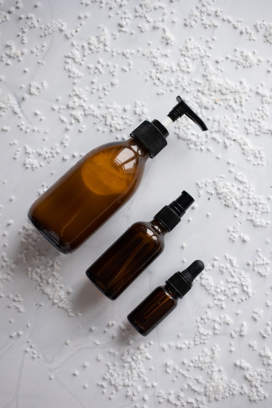Three amber glass skincare bottles in different sizes on a pale surface