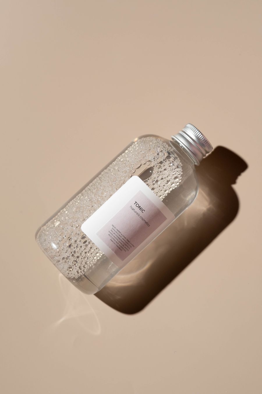 Clear cosmetic toner bottle on its side showing a band of fine bubbles in the liquid