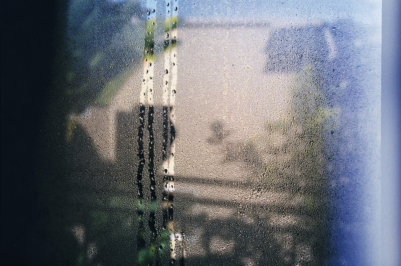Condensation film with run-down streaks covering a window pane in morning light