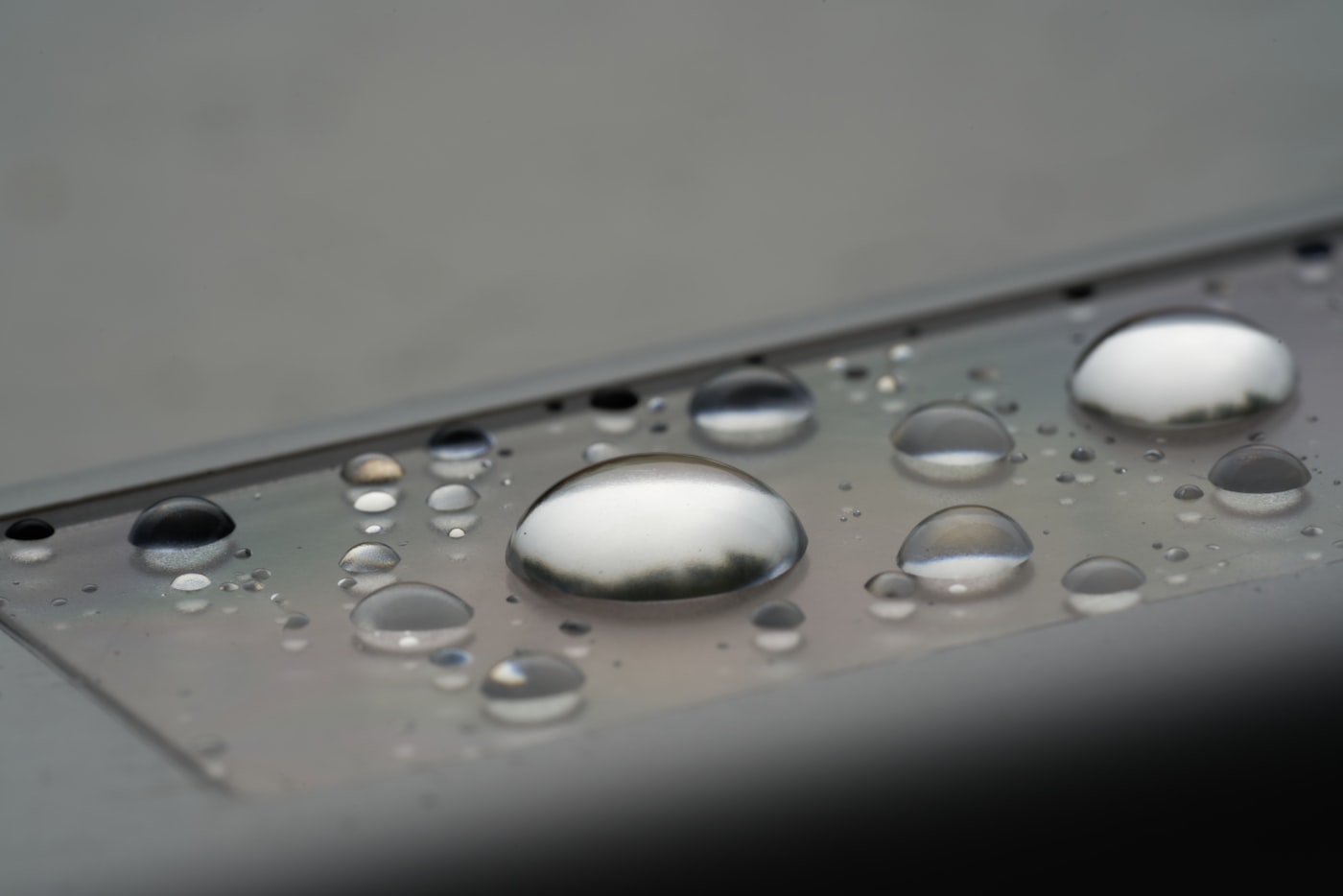 Beaded fluid droplets standing on a brushed metal panel