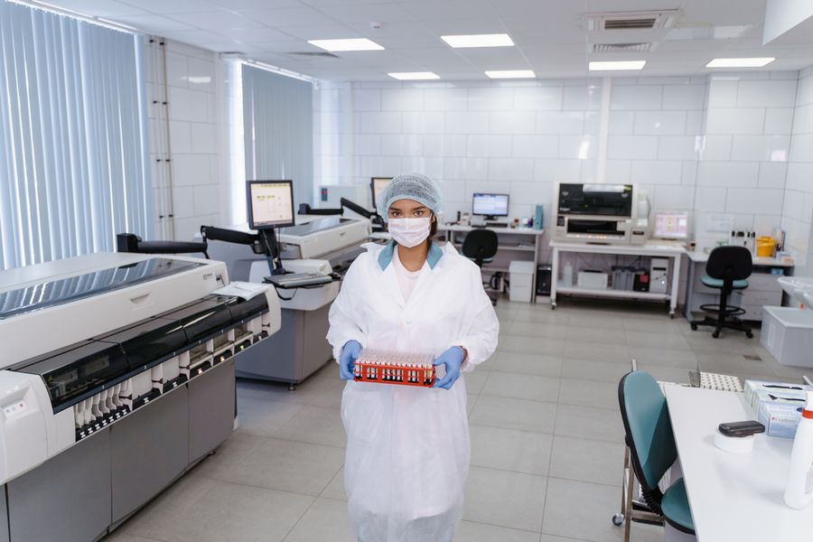 Laboratory technician carrying a rack of sample vials across a clean room