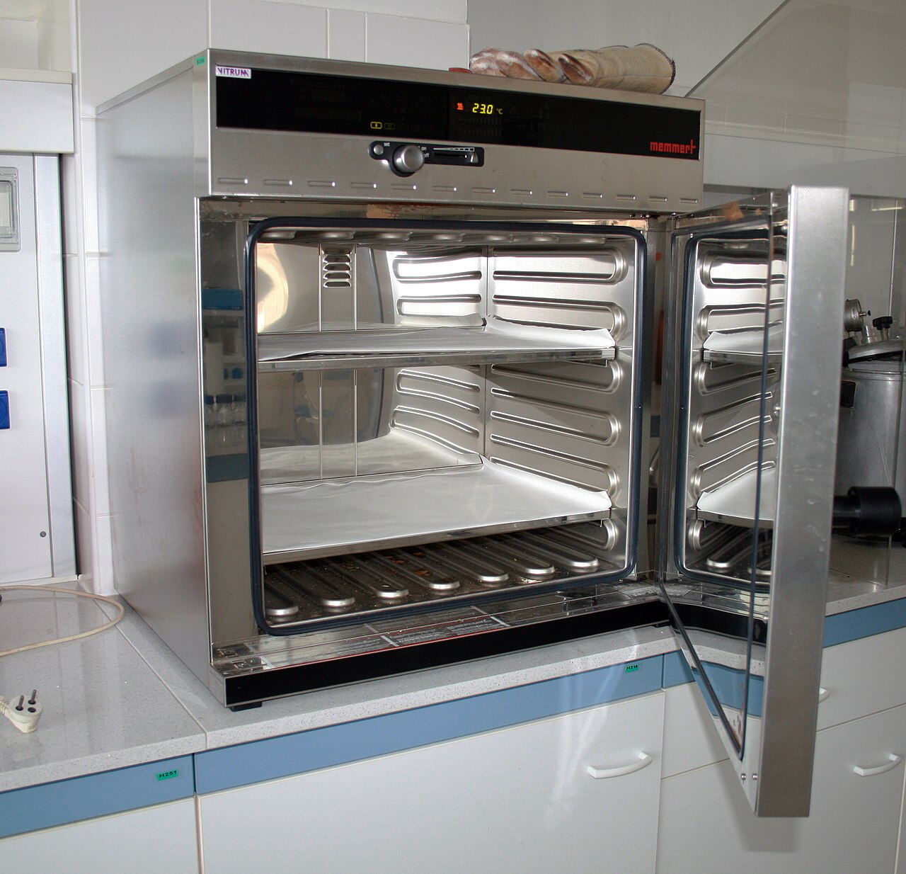 A laboratory dry heat oven with the door open, showing the shelves inside and a digital display reading 230 degrees Celsius