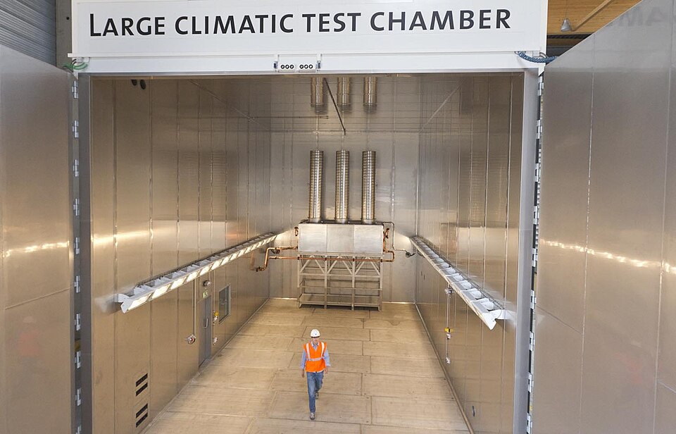 A large walk-in climatic test chamber with a person inside for scale, showing the conditioning ducts overhead