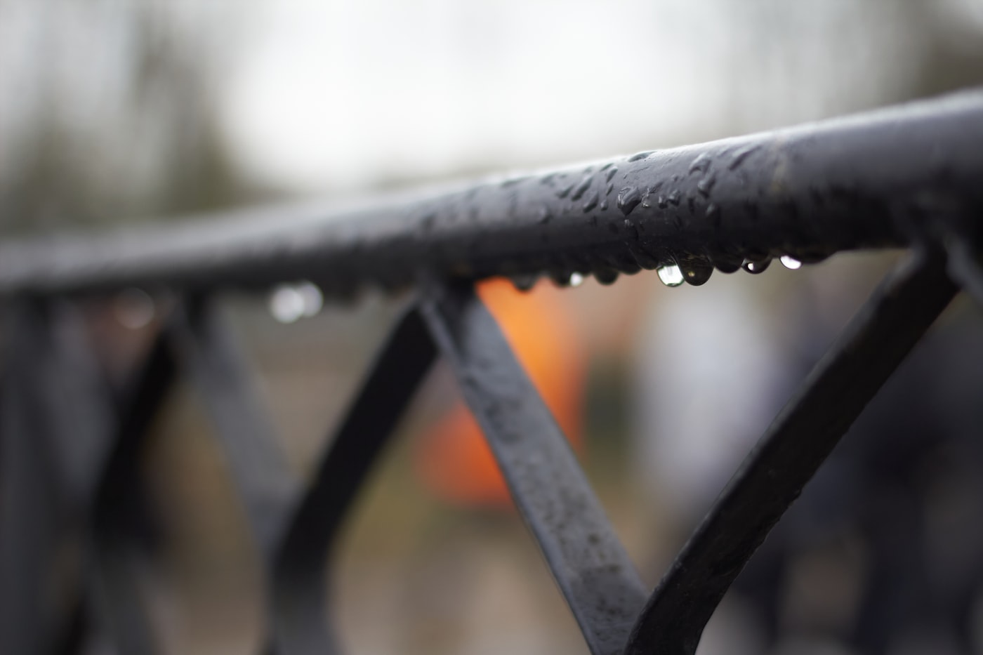 Raindrops clinging along the top of a wet iron railing