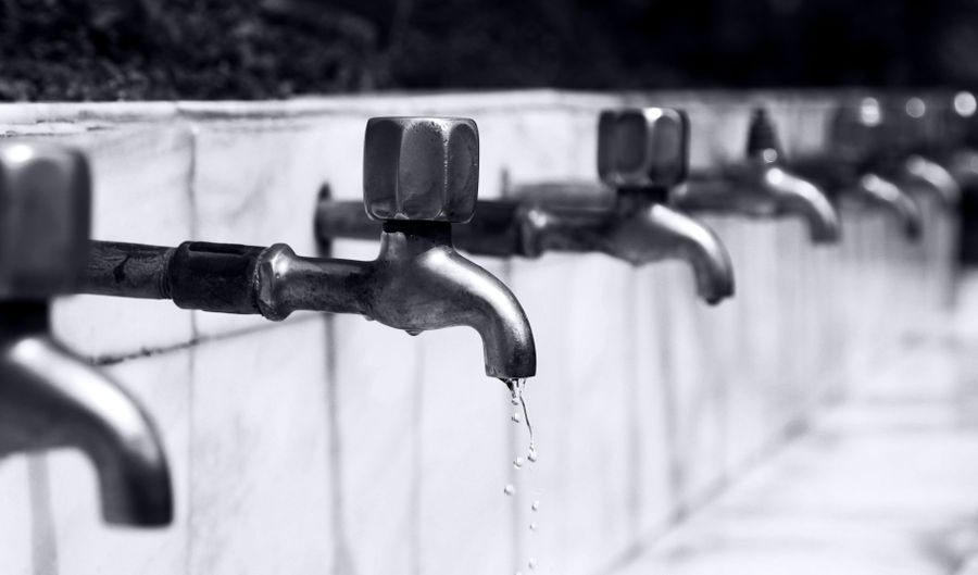 A row of metal water taps with one dripping