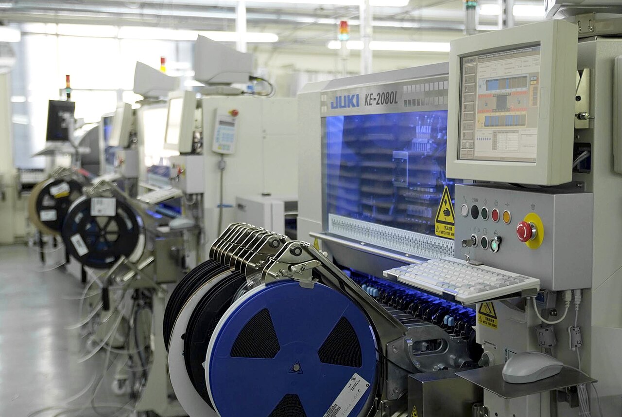 An electronics production line with surface-mount placement machines and component reels stretching back into the factory