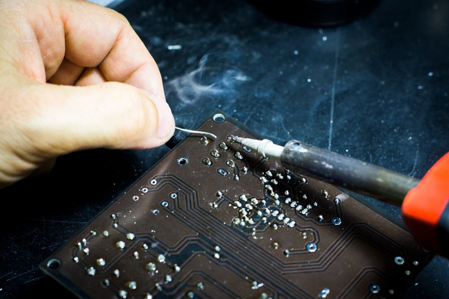 A hand soldering a printed circuit board, with a wisp of smoke