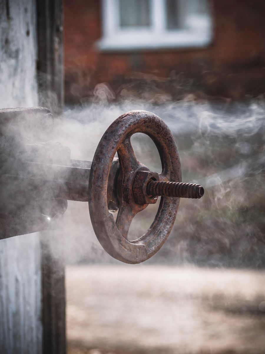 Steam rising around a rusty industrial valve wheel