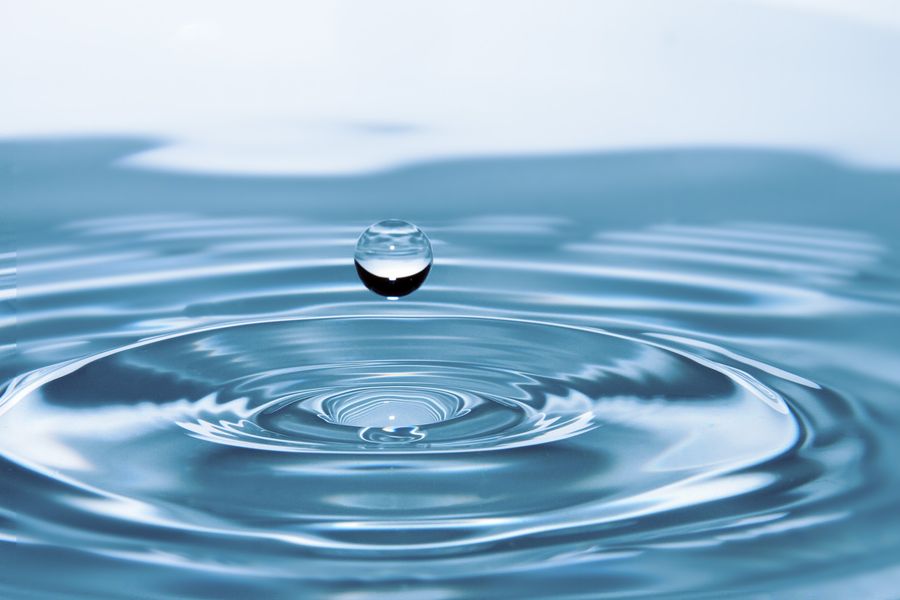 A single clear water drop above concentric ripples on a calm surface